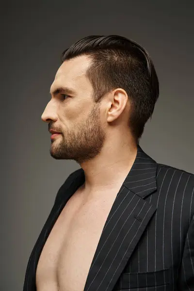 Portrait of handsome man in his 30s posing with bare chest in pinstripe suit on grey background — Stock Photo