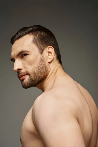 Porträt eines hemdlosen und gutaussehenden Mannes mit Borsten, der wegschaut, während er vor grauem Hintergrund posiert — Stockfoto