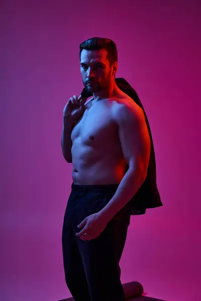 Muscular man in his 30s posing with bare chest in pants and holding blazer on purple background — Stock Photo