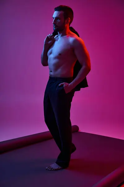 Shirtless man with bare chest and bristle holding jacket while posing with hand in pocket on purple — Stock Photo