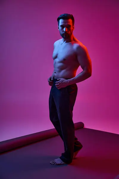 Homme séduisant et torse nu posant en pantalon à rayures sur fond violet avec des lumières rouges et bleues — Photo de stock