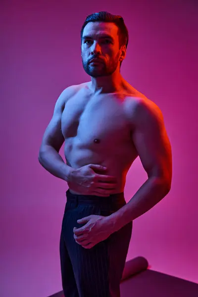 Красивый мужчина с обнаженной грудью, позирующий в полосатых брюках на фиолетовом фоне с красными огнями — стоковое фото