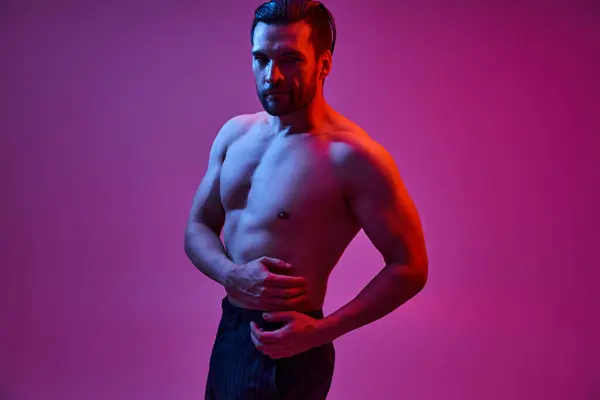 Homme séduisant avec poitrine nue sexy posant en pantalon à rayures sur fond violet avec des lumières rouges — Photo de stock