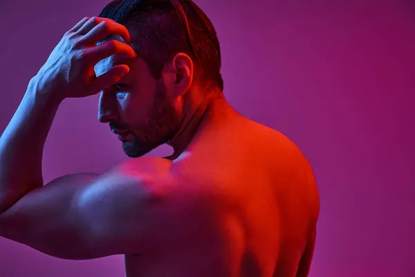 Portrait of muscular and shirtless man posing on purple background with red and blue lights — Stock Photo