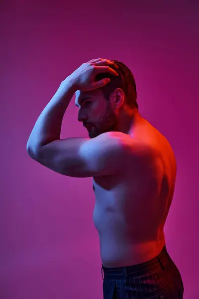 Seductive man with bare chest posing with hand near hair on purple backdrop with red lights — Stock Photo