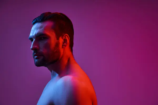 Retrato de homem sexy e muscular com cerda posando no fundo roxo com luzes vermelhas e azuis — Fotografia de Stock