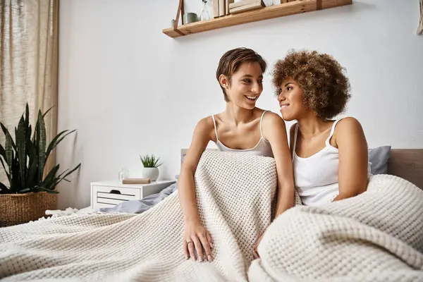 Glücklich afrikanisch-amerikanische Frau mit lockigem Haar sitzt mit Freundin auf dem Bett in der Früh, Romantik — Stockfoto