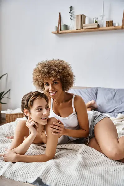 Joyeuse femme afro-américaine étreignant petite amie tout en étant couché ensemble sur le lit, l'intimité et l'amour — Photo de stock
