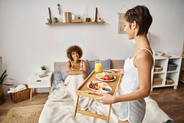 Vassoio donna felice con frittelle e bicchiere di succo d'arancia vicino alla ragazza, colazione a letto — Foto stock