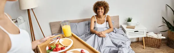 Felice donna afroamericana guardando fidanzata con pancake sul vassoio, colazione nel banner letto — Foto stock