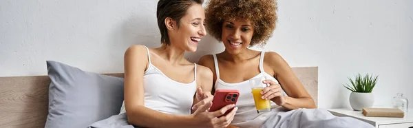 Heureuse lesbienne femme rire et en utilisant smartphone près afro-américaine petite amie, bannière — Photo de stock