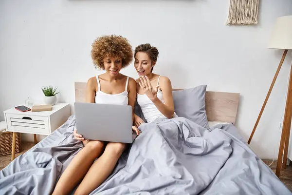 Heureuse fiancée femme montrant bague sur doigt pendant appel vidéo près de lesbienne afro-américaine fiancée — Photo de stock