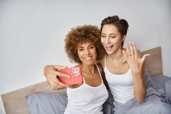 Excité et engagé interracial lesbienne couple prendre selfie sur smartphone à la maison, bague de fiançailles — Photo de stock