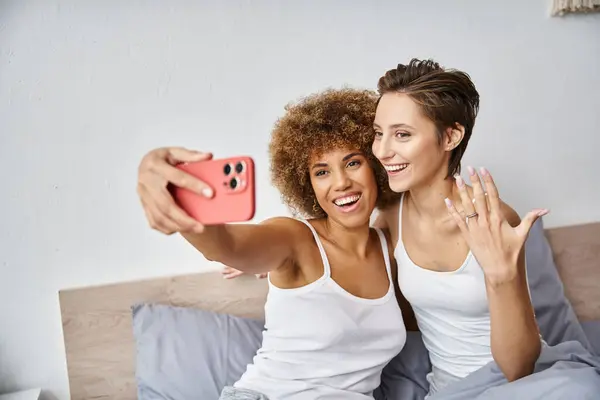 Happy and engaged interracial lesbian couple taking selfie on smartphone at home, engagement ring — Stock Photo