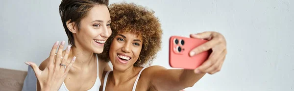 Feliz y comprometido interracial lesbianas pareja tomando selfie en smartphone en casa, pancarta - foto de stock