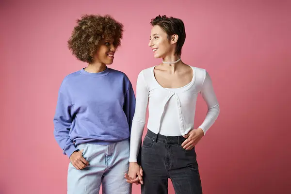Felice interrazziale lesbiche donne tenendosi per mano mentre in piedi su sfondo rosa, lgbtq coppia — Foto stock