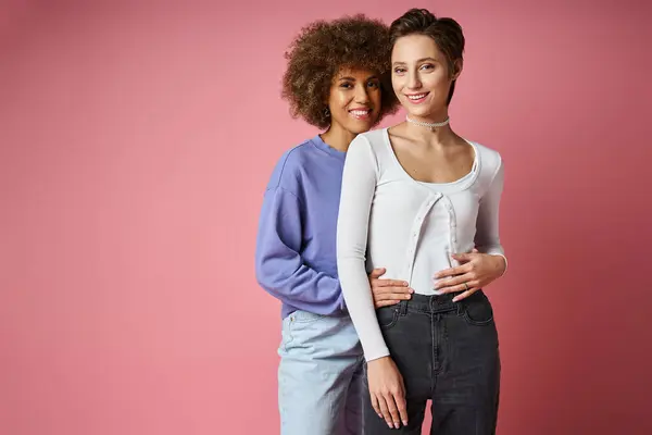Joyful multicultural lesbian women embracing while standing on pink background, lgbtq couple — Stock Photo