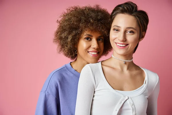 Joyful multicultural lesbian couple looking at camera together on pink background, lgbtq love — Stock Photo