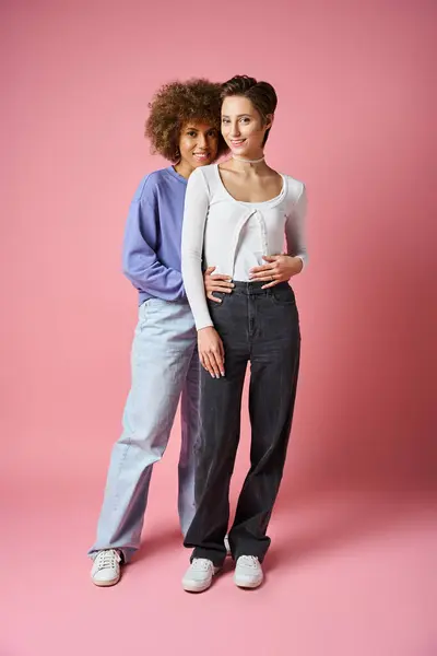 Позитивные многокультурные лесбиянки обнимаются, стоя на розовом фоне, lgbtq пара — стоковое фото