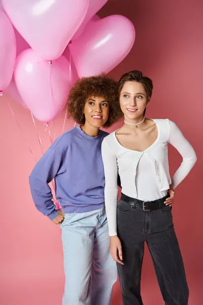 Dreamy multicultural lesbian couple smiling near pink heart shaped balloons, Saint Valentines day — Stock Photo