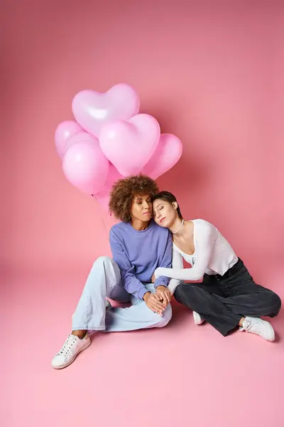 Молода багатокультурна пара лесбіянок, що сидить біля рожевих кульок у формі серця, день Святого Валентина — стокове фото