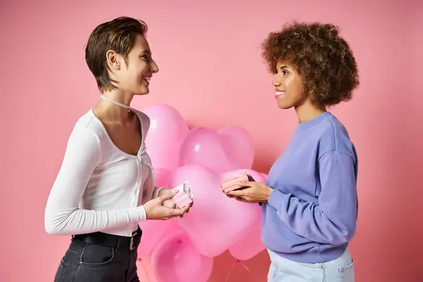 Glückliches multikulturelles lesbisches Paar tauscht am Valentinstag Geschenke in der Nähe herzförmiger Luftballons aus — Stockfoto