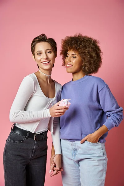 Glückliche lesbische Frau hält Geschenk und Hand einer afrikanisch-amerikanischen Freundin am Valentinstag, rosa — Stockfoto