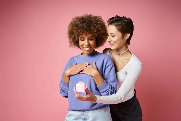 Cheerful lesbian woman giving present to amazed african american girlfriend on Valentins day — Stock Photo
