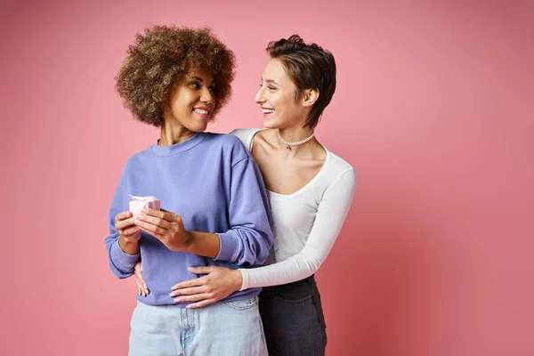 Cheerful lesbian woman looking at happy african american girlfriend with present on Valentins day — Stock Photo