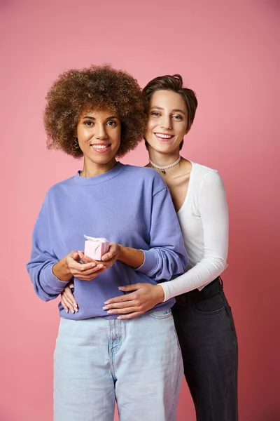 Cheerful lesbian woman hugging happy african american girlfriend with present on Valentins day — Stock Photo