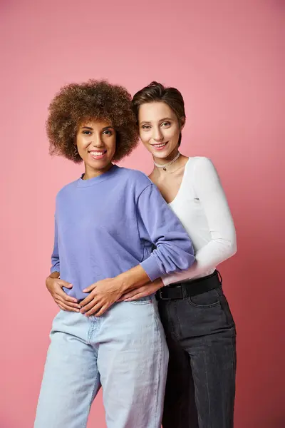 Smiling lesbian woman embracing african american girlfriend in casual clothes on pink background — Stock Photo