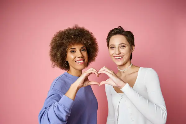 Glückliches multikulturelles und lesbisches Paar zeigt Herzzeichen mit Händen auf rosa Hintergrund, lgbtq love — Stockfoto