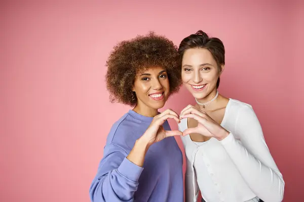 Fröhliches multikulturelles und lesbisches Paar zeigt Herzzeichen mit Händen auf rosa Hintergrund, lgbtq love — Stockfoto