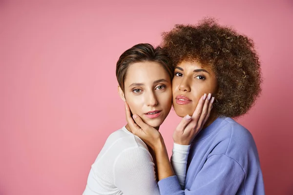 Portrait de couple lesbienne multiculturel en vêtements décontractés regardant la caméra sur fond rose — Photo de stock