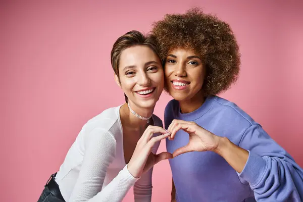 Glückliches multikulturelles lgbtq Paar zeigt Herzzeichen mit Händen auf rosa Hintergrund, Liebe — Stockfoto