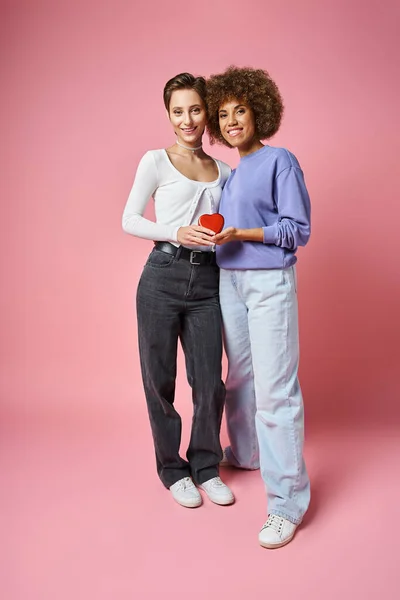 Счастливая мультикультурная пара lgbtq держа красную коробку в форме сердца на розовом фоне, День Святого Валентина — стоковое фото
