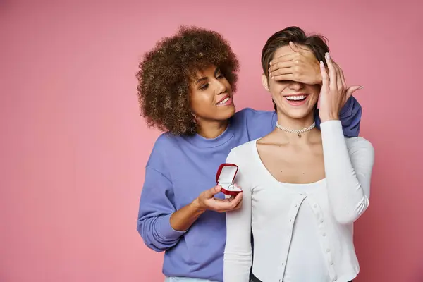 Africaine américaine femme tenant boîte avec bague de fiançailles et couvrant les yeux de petite amie heureuse — Photo de stock