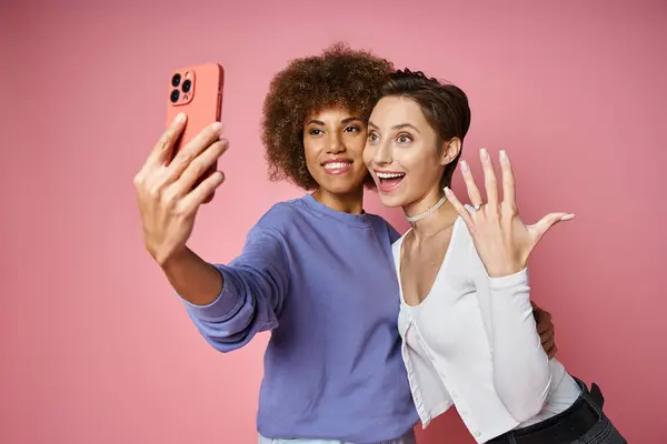 Gaie lesbienne femme montrant bague de fiançailles sur doigt tout en prenant selfie avec fiancée sur rose — Photo de stock
