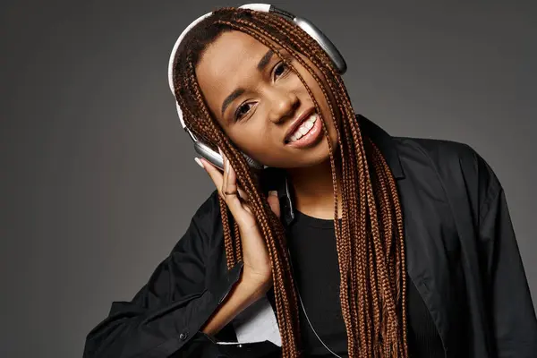 Portrait of happy african american girl in dreadlocks listening music in wireless headphones on grey — Stock Photo
