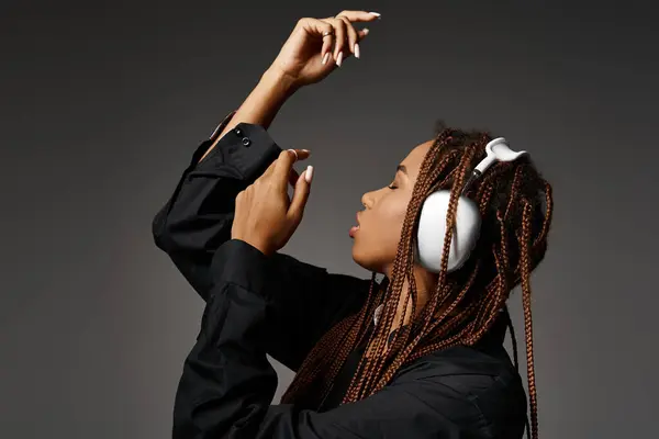Artistic african american girl in 20s with dreadlocks listening music in headphones on grey backdrop — Stock Photo