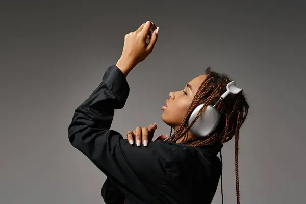 African american woman with dreadlocks listening music in headphones and looking away on grey — Stock Photo
