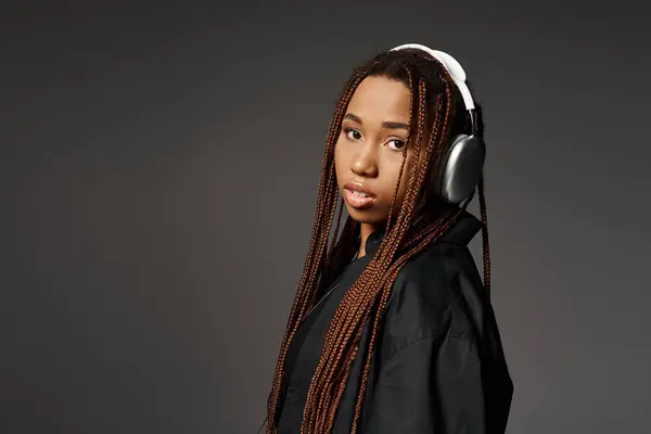 Pretty african american girl with dreadlocks listening music in headphones on grey background — Stock Photo