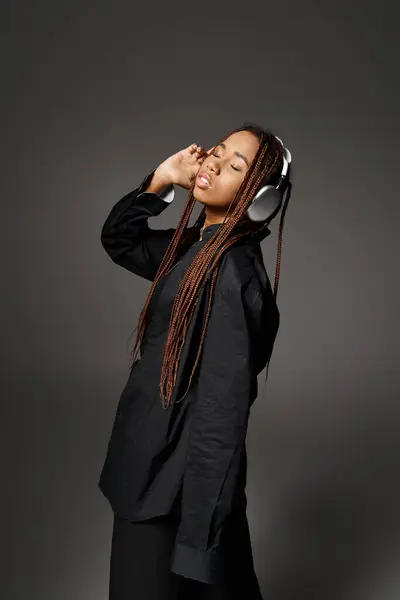 Menina americana africana elegante com dreadlocks ouvir música em fones de ouvido no fundo cinza — Fotografia de Stock