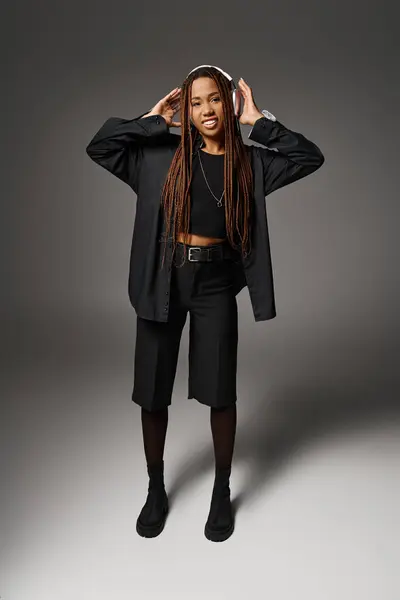 Sorrindo mulher afro-americana com dreadlocks ouvir música em fones de ouvido em fundo cinza — Fotografia de Stock