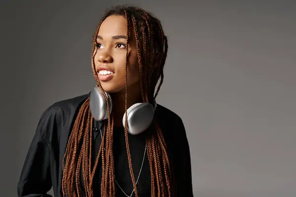 Happy african american woman with dreadlocks standing in headphones and looking away on gray — Stock Photo