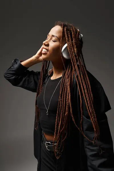 Positive african american girl in 20s with dreadlocks listening music in headphones on grey backdrop — Stock Photo