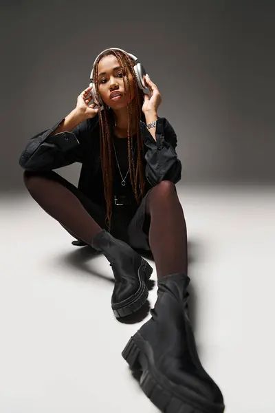 Stylish african american woman in 20s with dreadlocks enjoying music in headphones on grey — Stock Photo