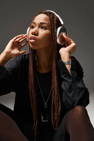 African american woman in 20s with dreadlocks enjoying music in trendy headphones on grey — Stock Photo