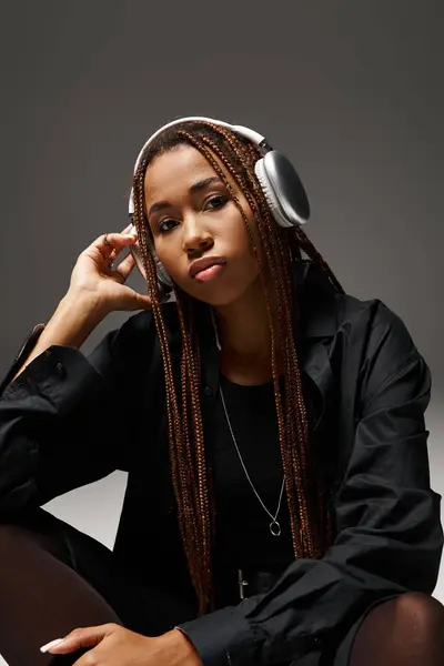 Young african american woman in 20s with dreadlocks listening music in stylish headphones on grey — Stock Photo