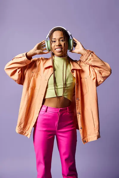 Happy african american girl in wireless headphones and vibrant casual attire on purple background — Stock Photo
